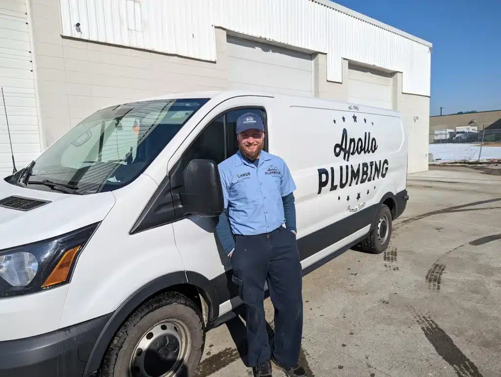 Plumber standing beside branded service van outdoors
